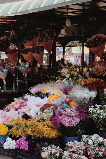 A vibrant flower stall displays an abundance of fresh floral arrangements at a market, with bouquets featuring a variety of blooms including roses, daisies, and chrysanthemums in shades of pink, white